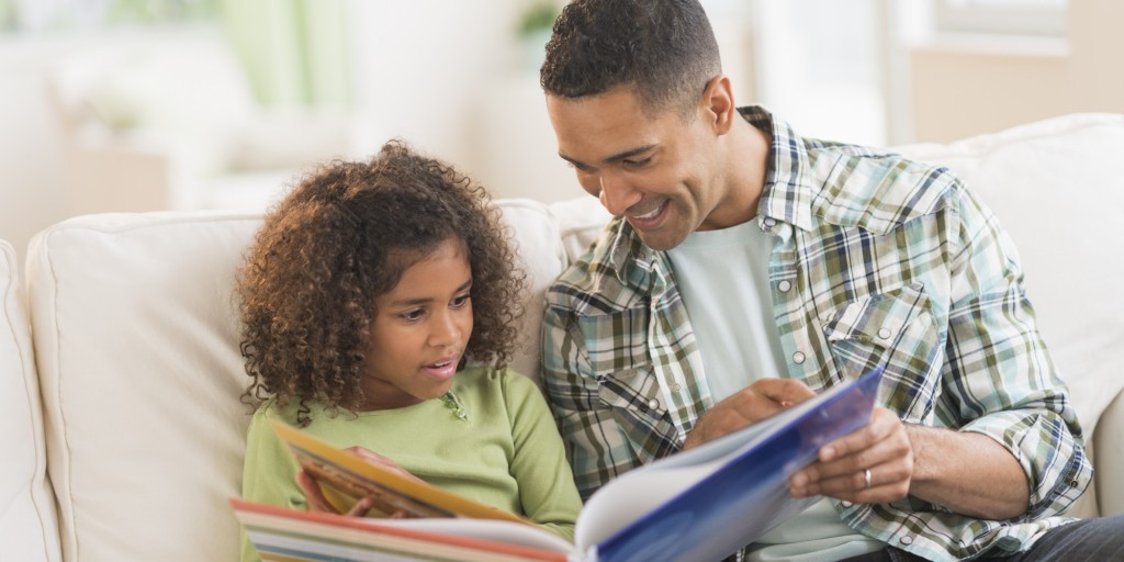 Father with daughter (6-7) reading book on sofa